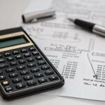 calculadora, papel e caneta sobre a mesa