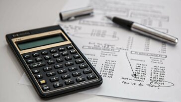 calculadora, papel e caneta sobre a mesa